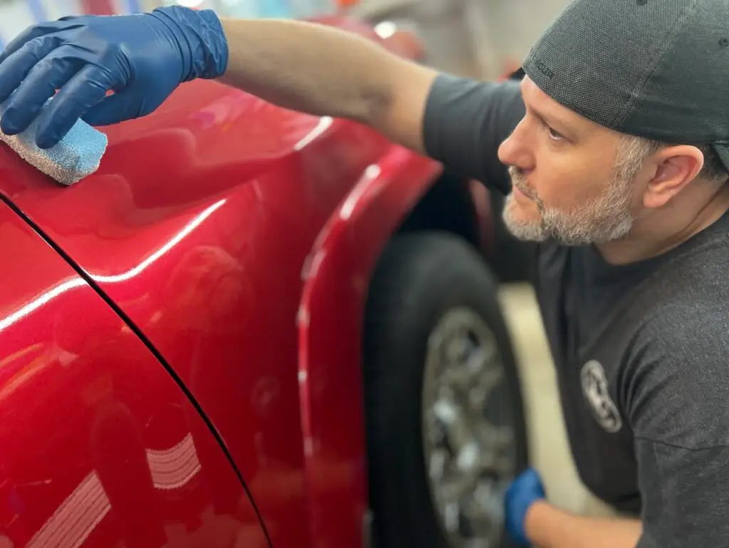 man ceramic coating a red vehicle